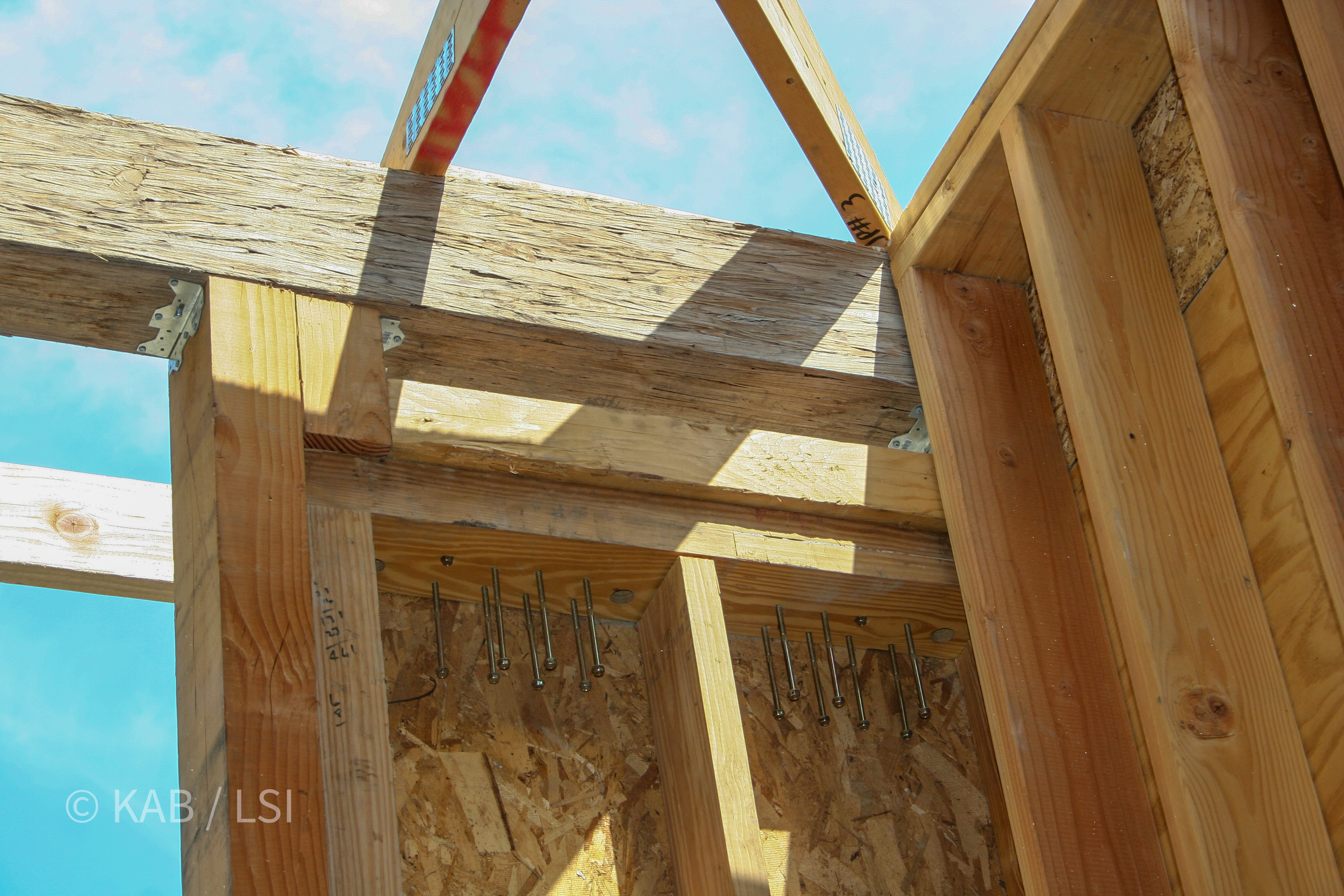 Hold-down bolts protruding from sheathing at the ridge — seismic tie-down detail © KAB/LSI