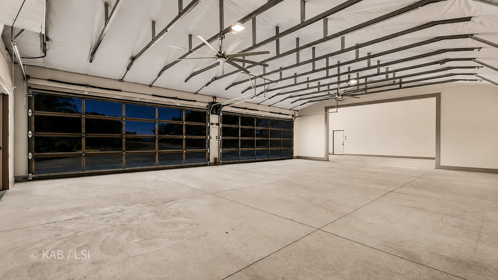 The empty interior of a hillside RV garage at dusk — exposed steel rafters, big-blade industrial fans, polished concrete floor.