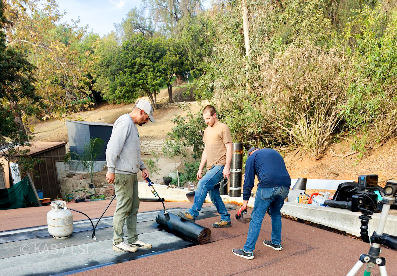 Racing the rain — a just-finished La Habra Heights outbuilding getting its torch-down roof before the rain hits the plywood. A crew worth watching, being watched.