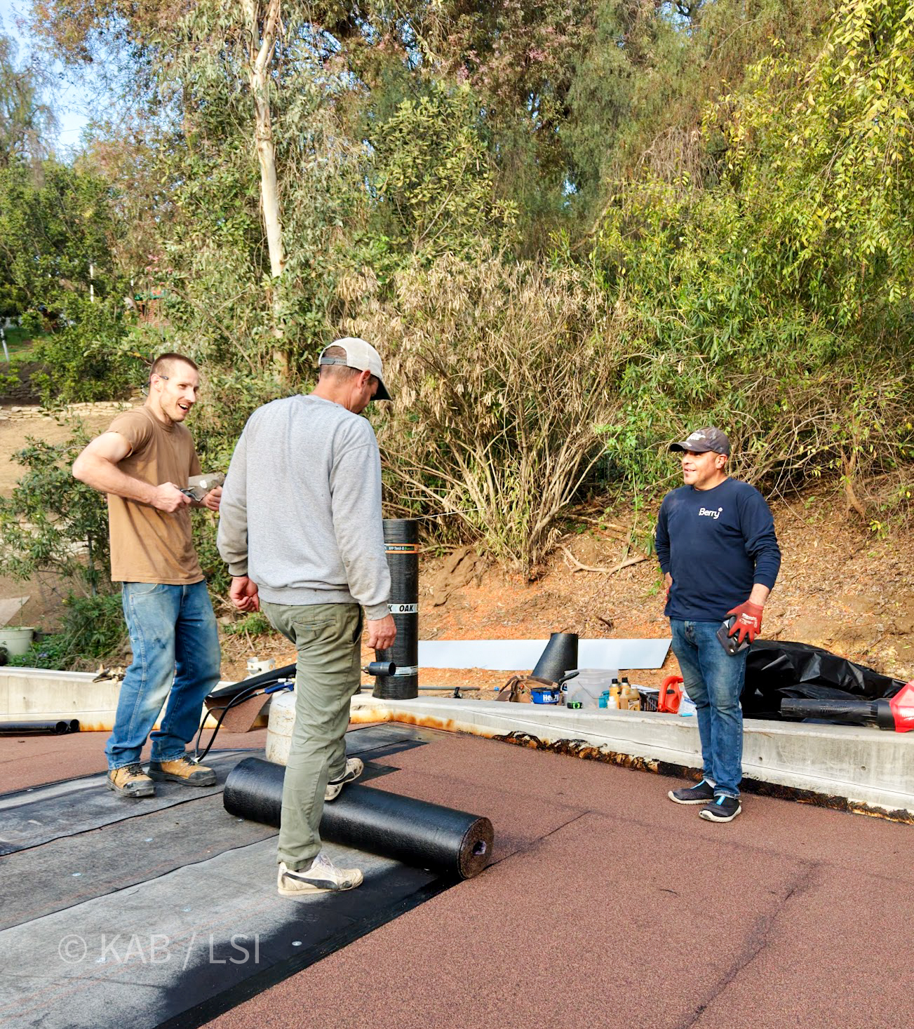 Three-man crew torch-down roofing a brand-new La Habra Heights hillside outbuilding ahead of an incoming storm, while being observed